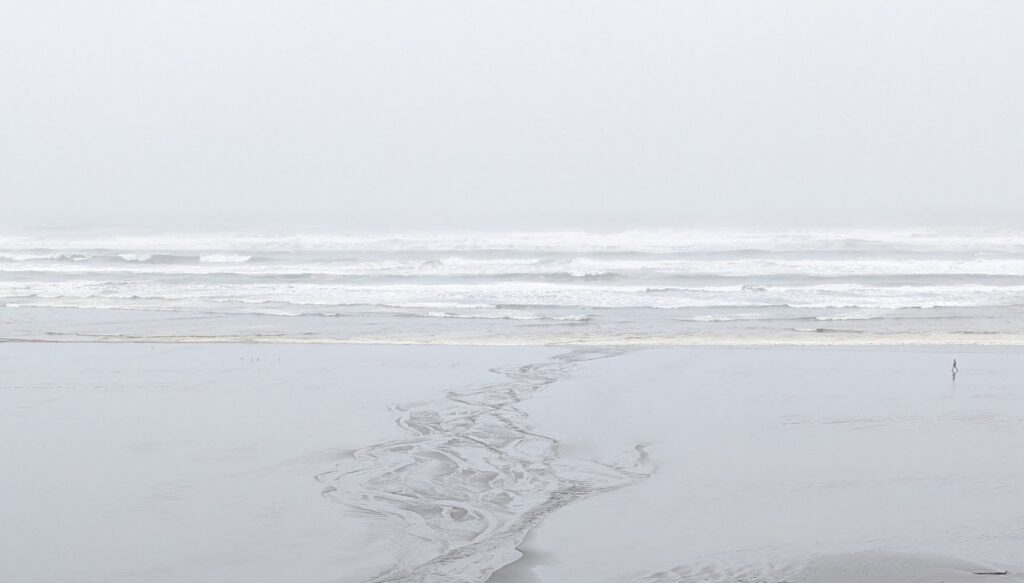 Very gray beach with one person walking in the distance.